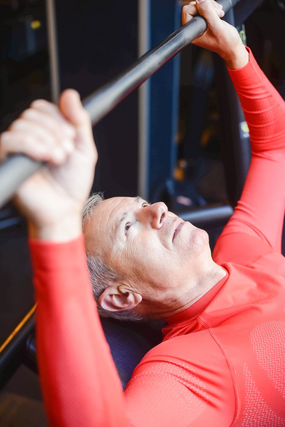 Close view of an older man pressing a barbell from a bench.