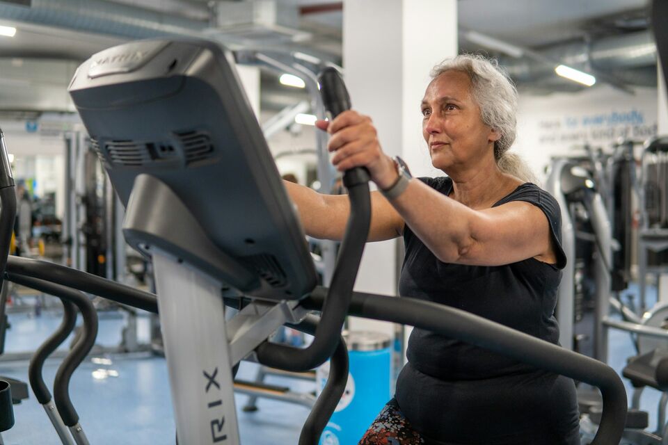 An older woman exercises on an elliptical machine in a gym.